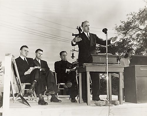 Groundbreaking ceremony with man speaking, three men and a woman organ player on outdoor platform