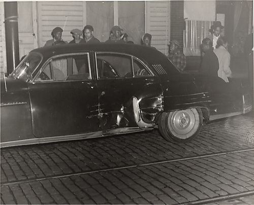 People standing beside dented Cadillac car on street
